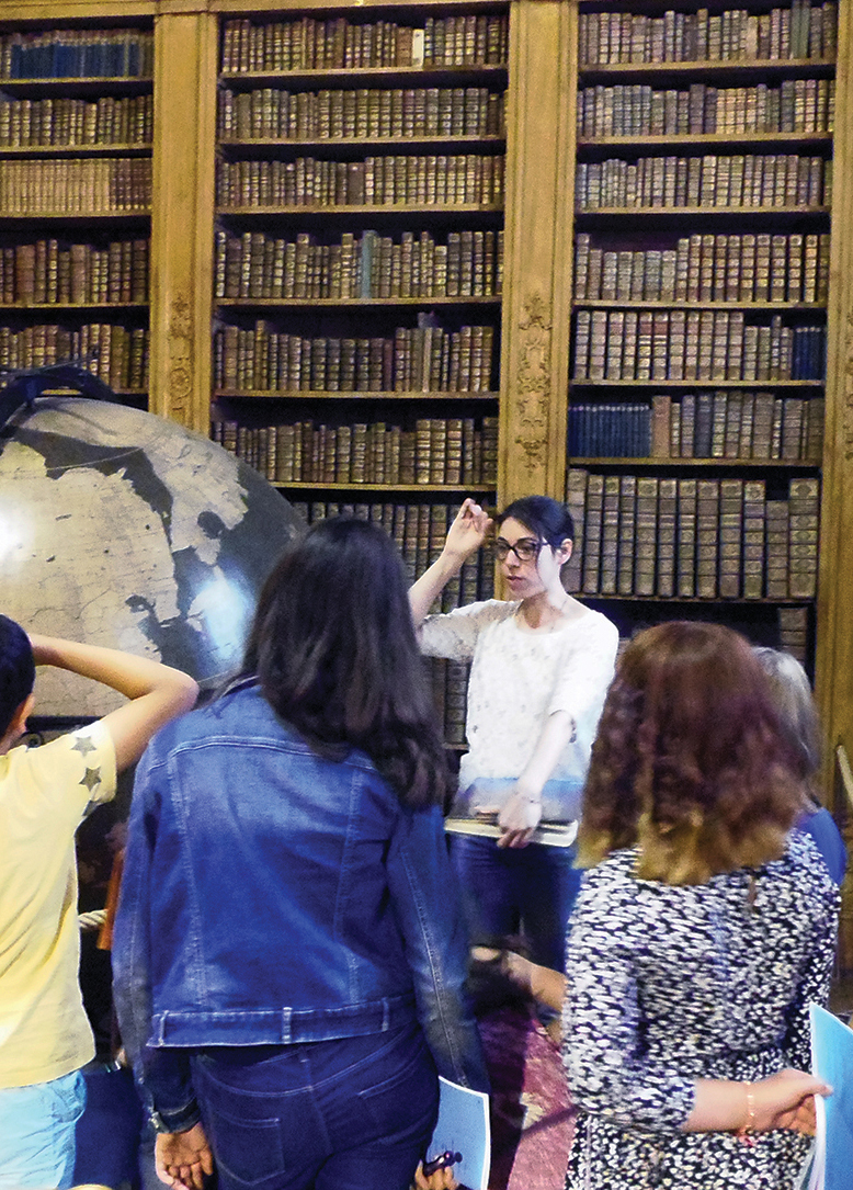 Une jeune bibliothécaire explique l'histoire de la bibliothèque vers les globes à un groupe de jeunes 
